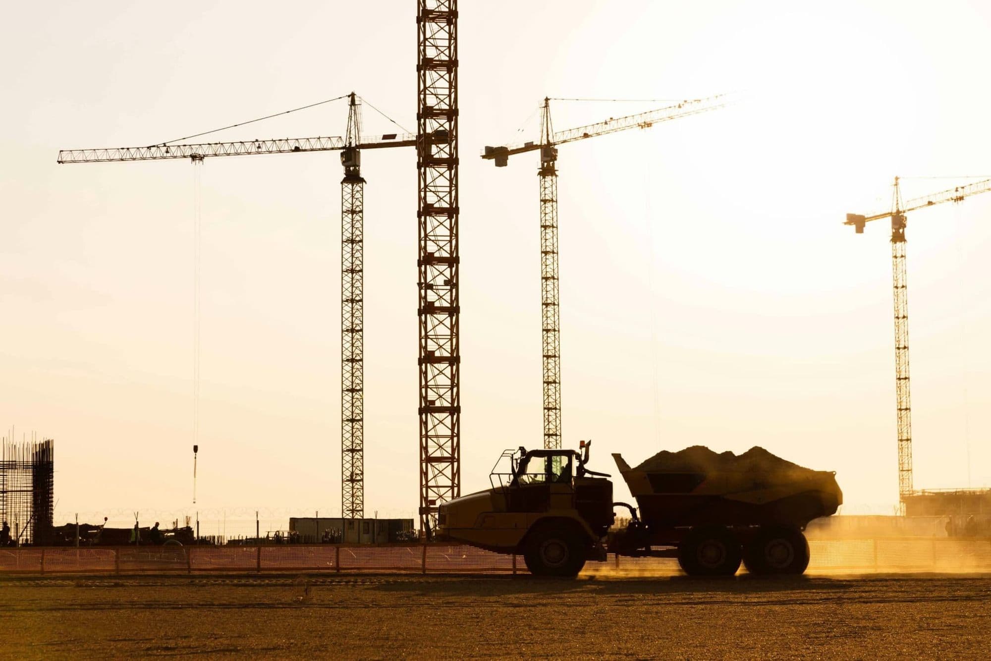 Tower cranes and site vehicles on a construction site at sunset