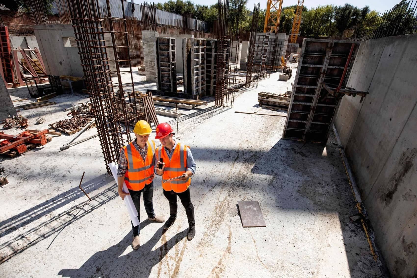 Two supervisors in hard hats and vests reviewing plans on site