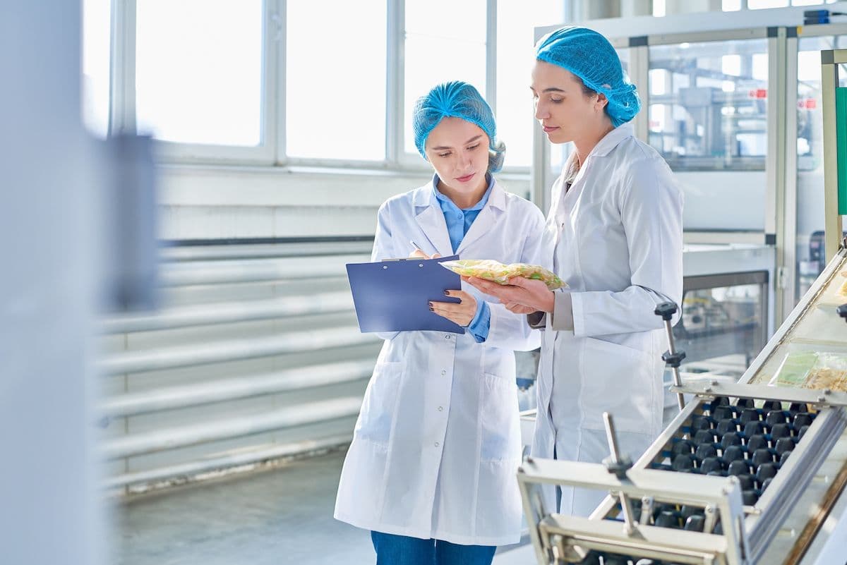 Two technologists reviewing compliance records on a clipboard in a factory